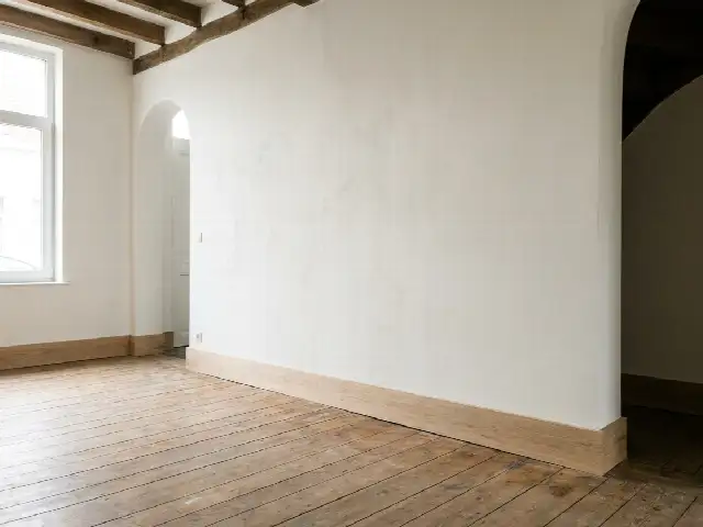 Opnieuw bepleisterde en geschilderde muur in een woonkamer met een nieuwe plint