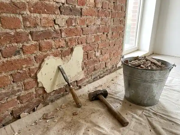 Oude pleister die onderaan een bakstenen binnenmuur wordt afgekapt